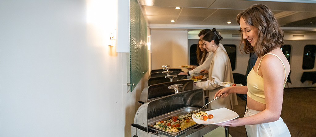 People taking food from buffet plates on the Magistic Lunch Cruise