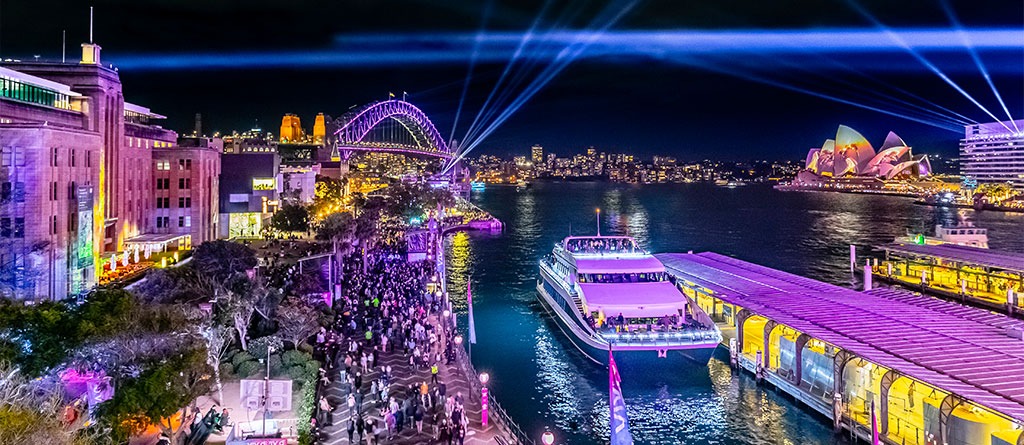 Aerial view of the harbour with vivid lights in the background and the Magistic Two Catamaran docked at the wharf